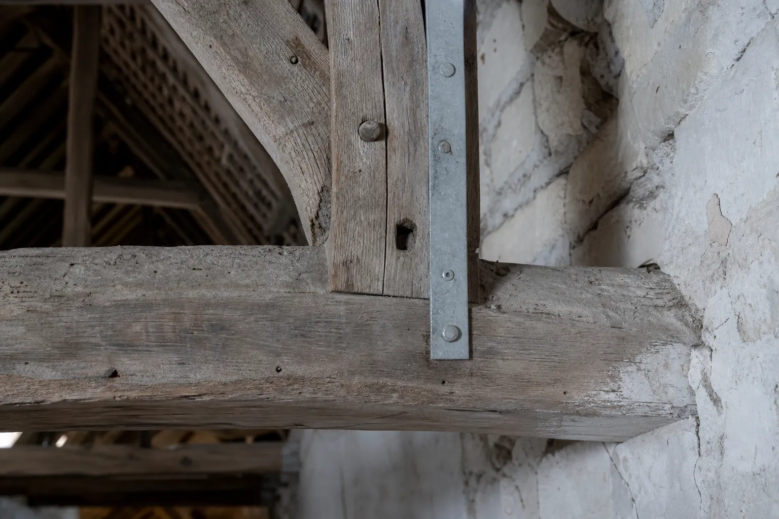 Détail d’un assemblage de ferme de charpente en chêne, tenon chevillé et feuillard galvanisé neuf fixé le long de l’assemblage