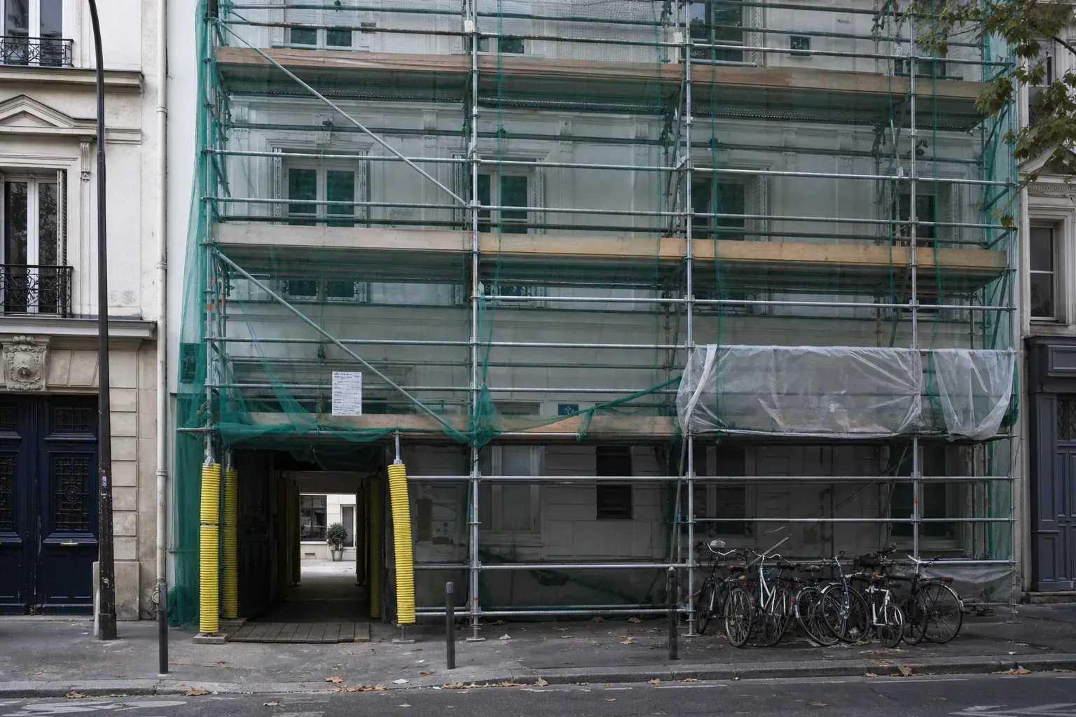 Échafaudage monté sur la façade d’un immeuble d’habitation occupé, filet de sécurité vert et entrée maintenue dégagée au rez-de-chaussée