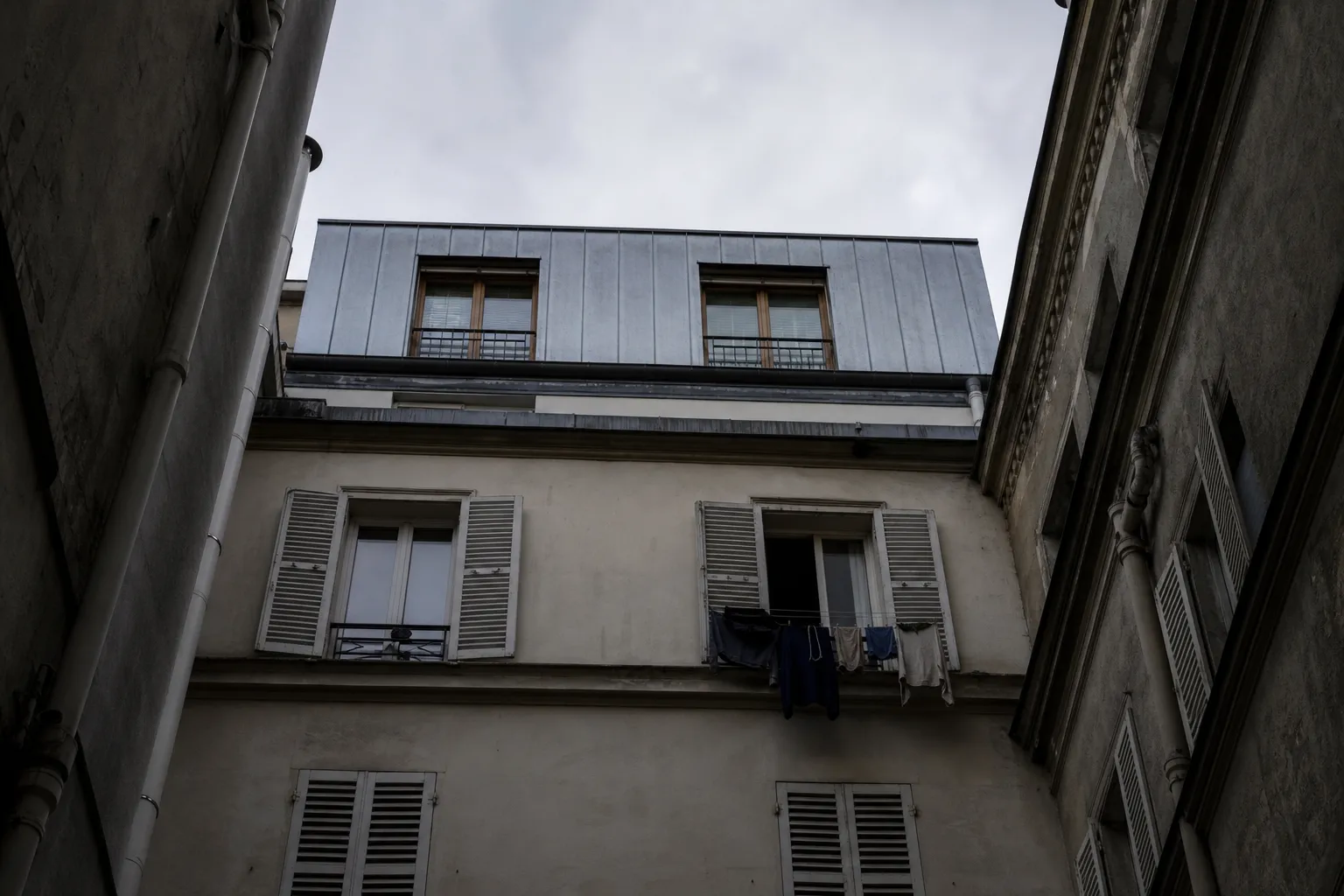 Vue depuis une cour parisienne vers le haut d’un immeuble ancien surmonté d’un étage neuf en zinc, légèrement en retrait