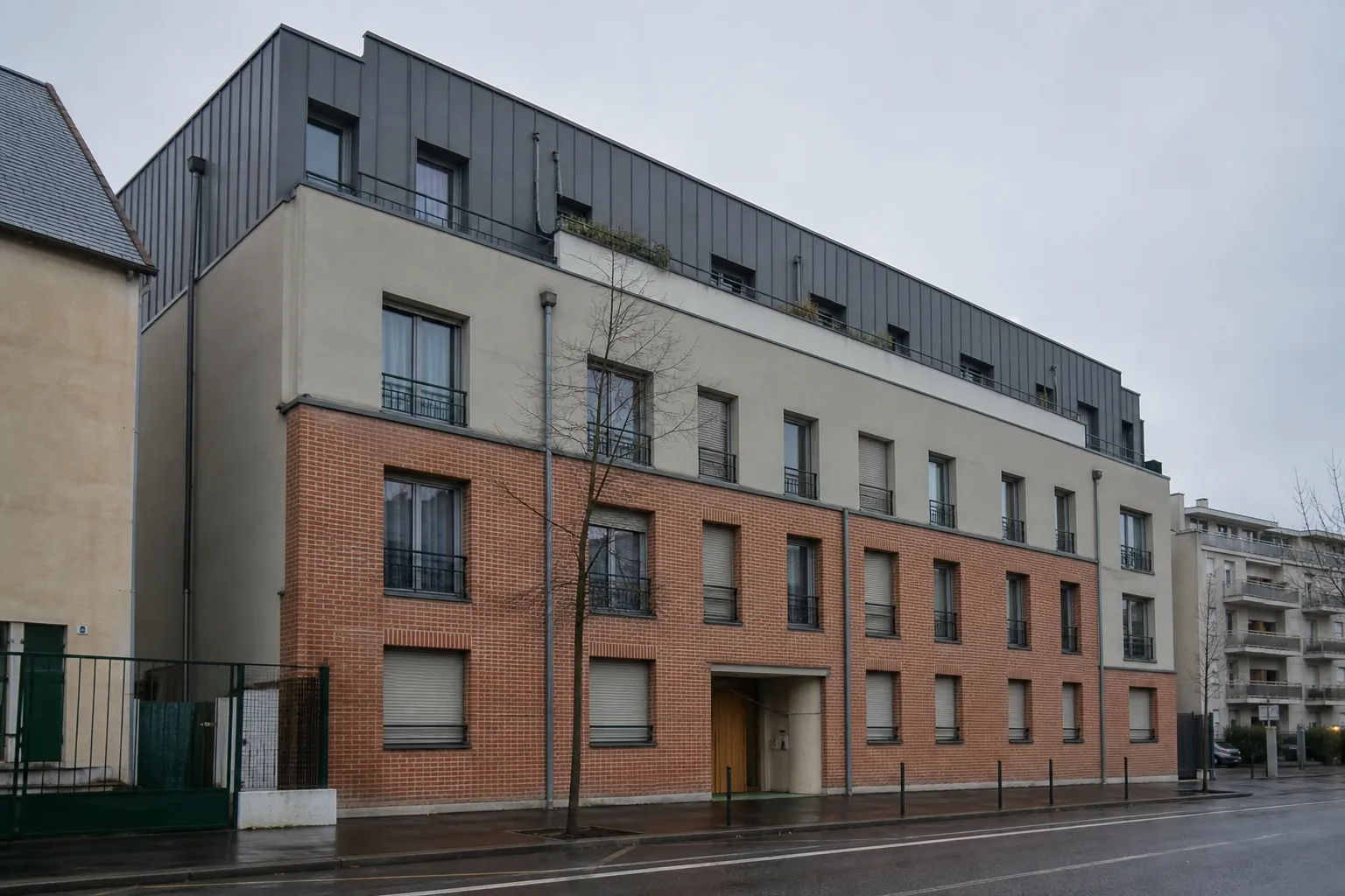 Immeuble de faubourg en brique et enduit de quatre étages surmonté d’un niveau supplémentaire en retrait bardé de métal sombre