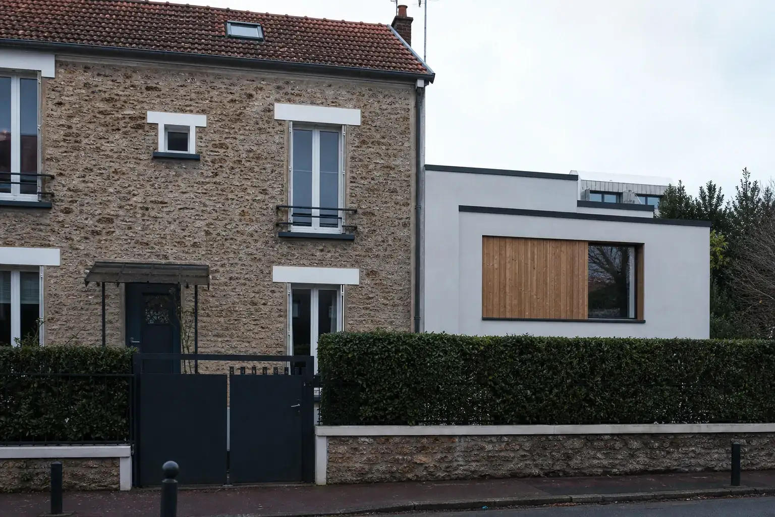 Maison de meulière de banlieue parisienne avec une extension récente à toit plat accolée sur le côté, haie basse devant